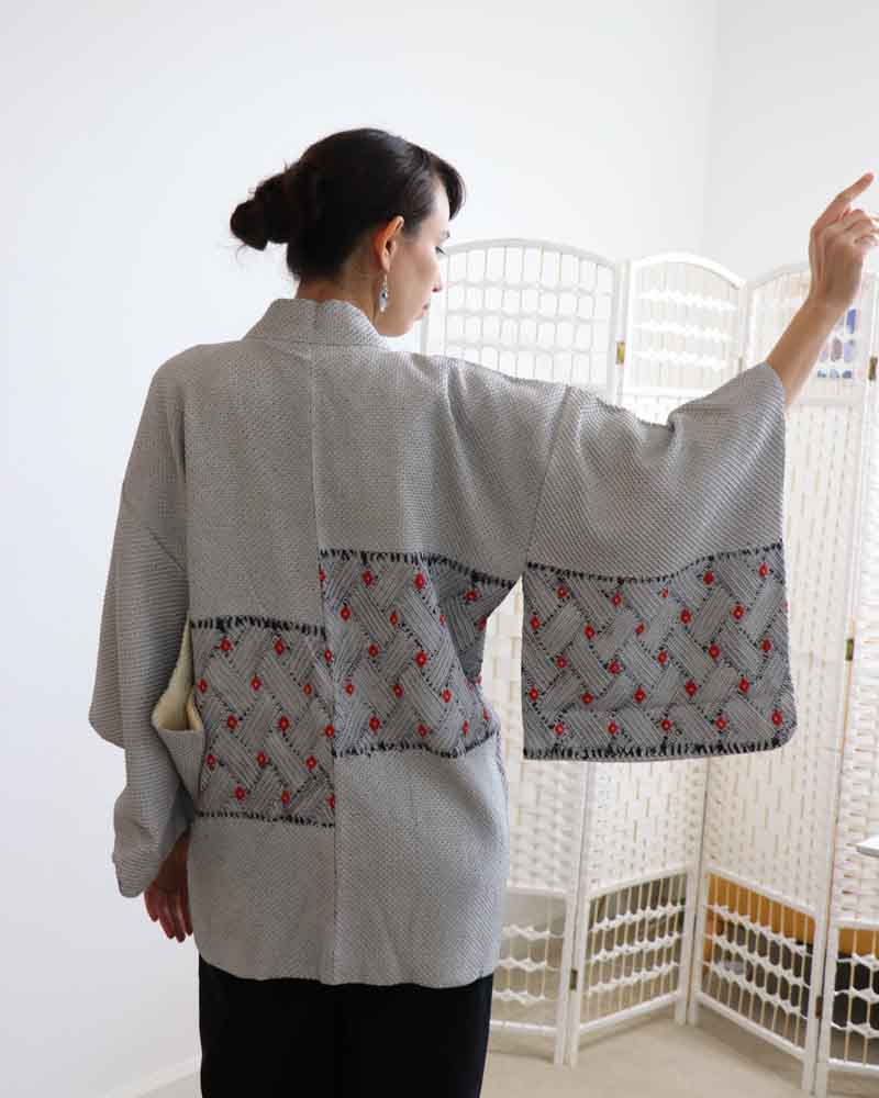 A woman wearing a blue and kimono, facing backwards and rising her right hand.