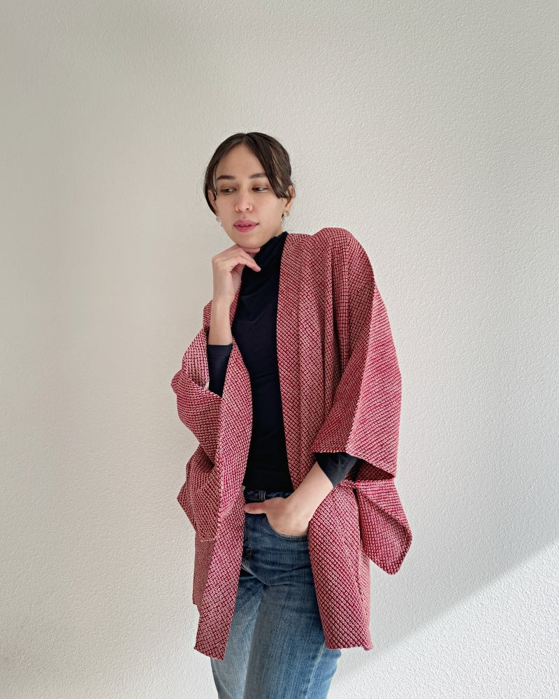 A front view of a woman wearing the Azuki All Shibori Haori Kimono Jacket, a product of the KIMONO ZEN brand, in a reddish hue with jeans.