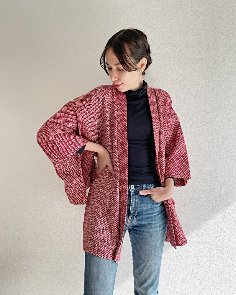 Front view of a woman wearing the Azuki All Shibori Haori Kimono Jacket from the KIMONO ZEN brand, reddish in hue, with jeans and a black turtleneck.