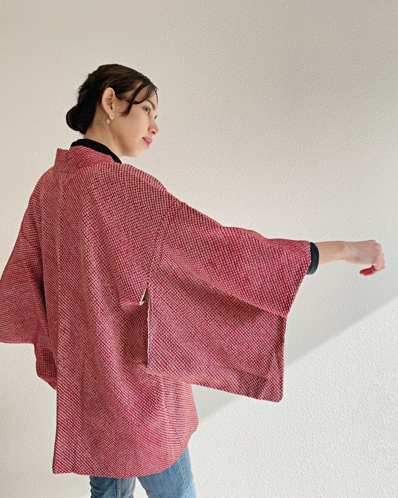 A woman wearing a reddish color with jeans and a black turtleneck is seen from behind.