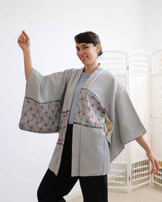 A woman wearing a kimono, facing forward and raising her right hand.