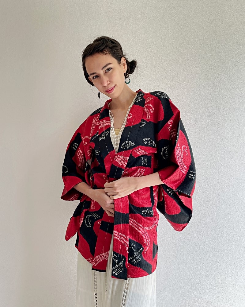 Front upper half of a woman wearing a Haori Kimono Jacket from the KIMONO ZEN brand in shades of black and red.