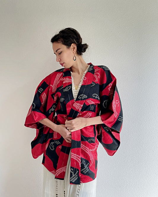 Front upper half of a woman wearing a Haori Kimono Jacket from the KIMONO ZEN brand in shades of black and red.