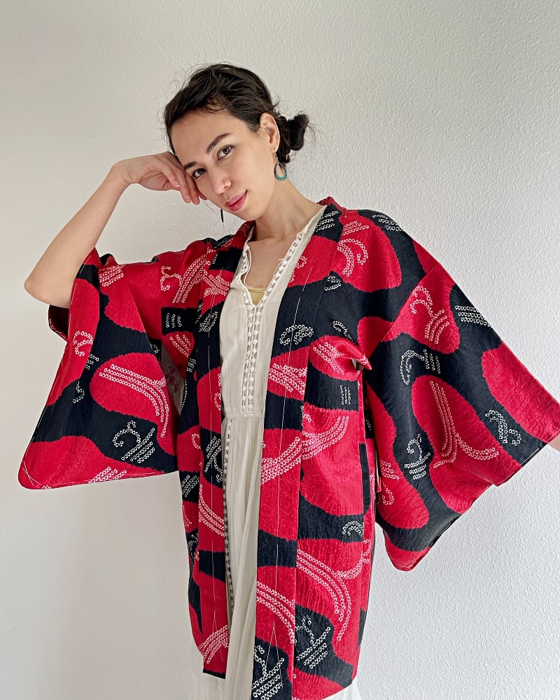 Front upper half of a woman wearing a Haori Kimono Jacket from the KIMONO ZEN brand in shades of black and red.