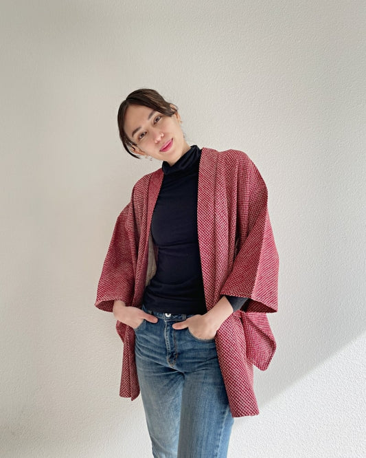 A front view of a woman wearing the Azuki All Shibori Haori Kimono Jacket, a product of the KIMONO ZEN brand, in a reddish hue with jeans.
