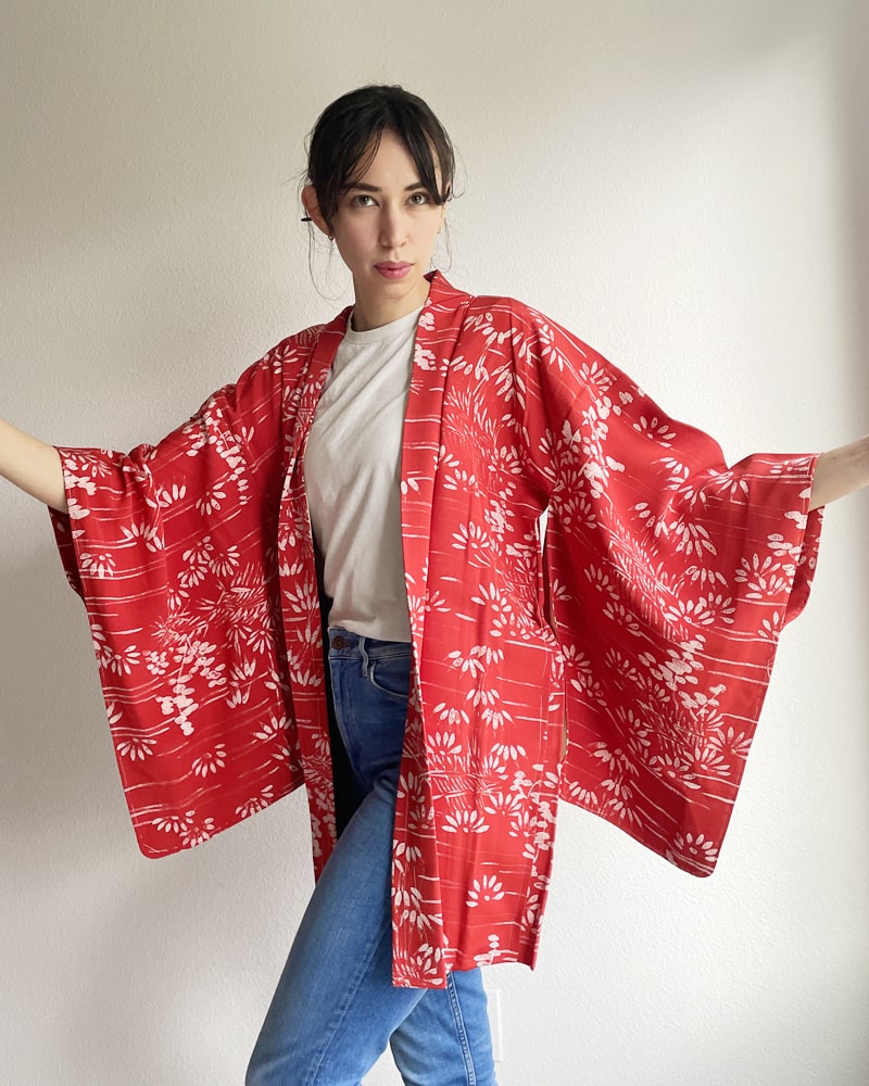A woman wearing a KIMONO ZEN brand Bamboo Forest Haori Kimono Jacket in a shade of red with jeans and a white T-shirt.