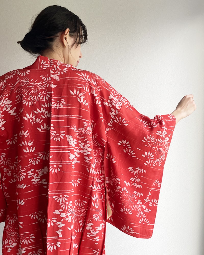 Back view of a woman wearing a Bamboo Forest Haori Kimono Jacket from the KIMONO ZEN brand in a shade of red with jeans and a white T-shirt.