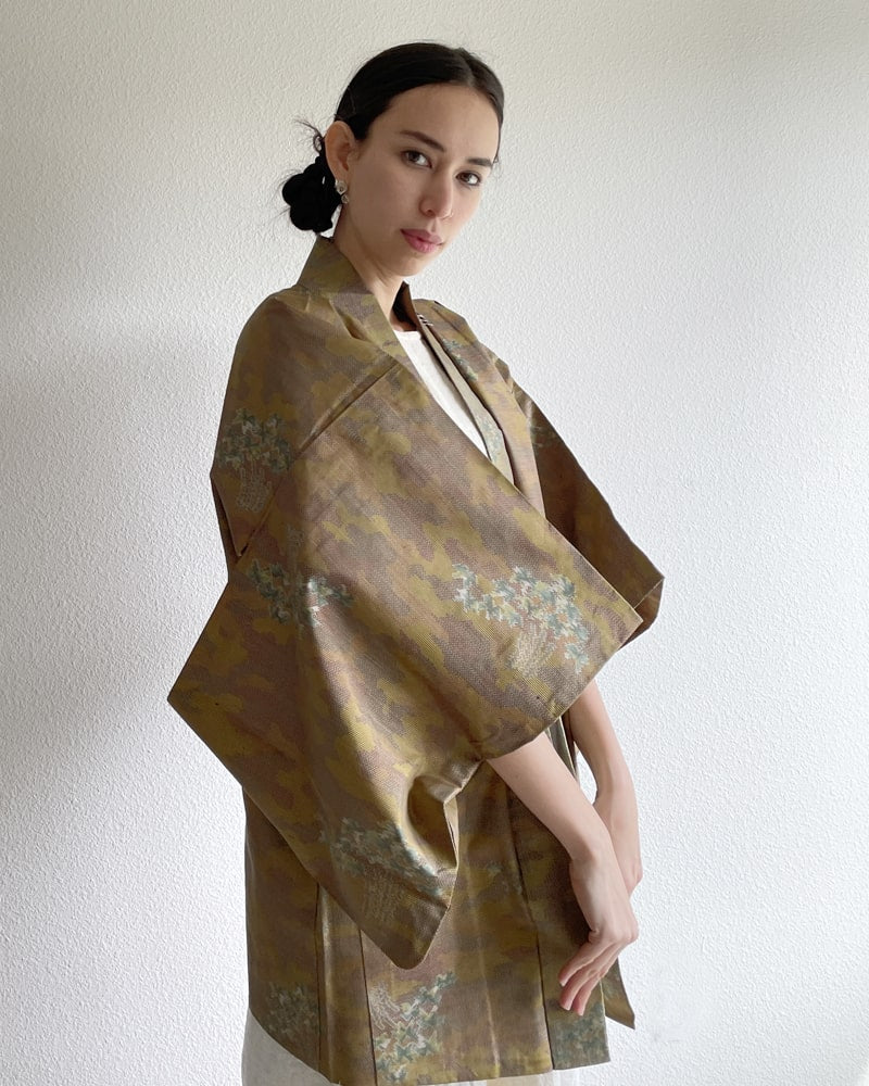 Front view of a woman wearing a KIMONO ZEN brand Bamboo Yellow Brown Oshima Tsumugi Haori Kimono Jacket with an ivory colored dress made of natural material in ochre color.