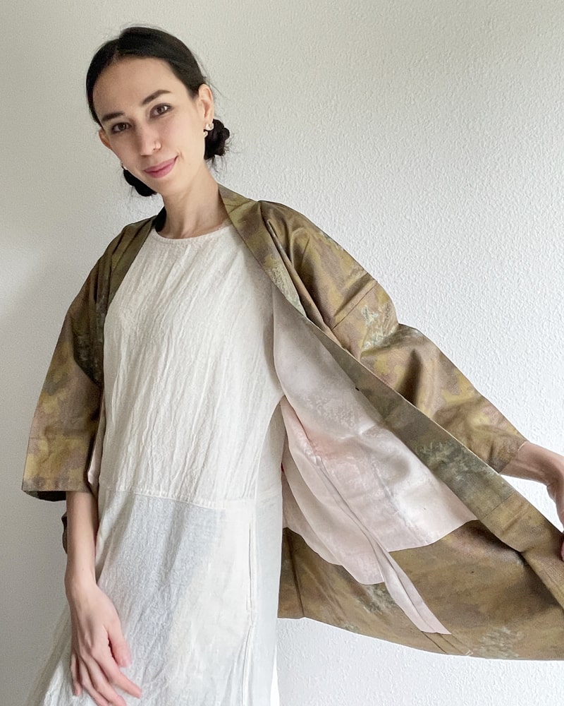 Front view of a woman wearing a KIMONO ZEN brand Bamboo Yellow Brown Oshima Tsumugi Haori Kimono Jacket with an ivory colored dress made of natural material in ochre color.