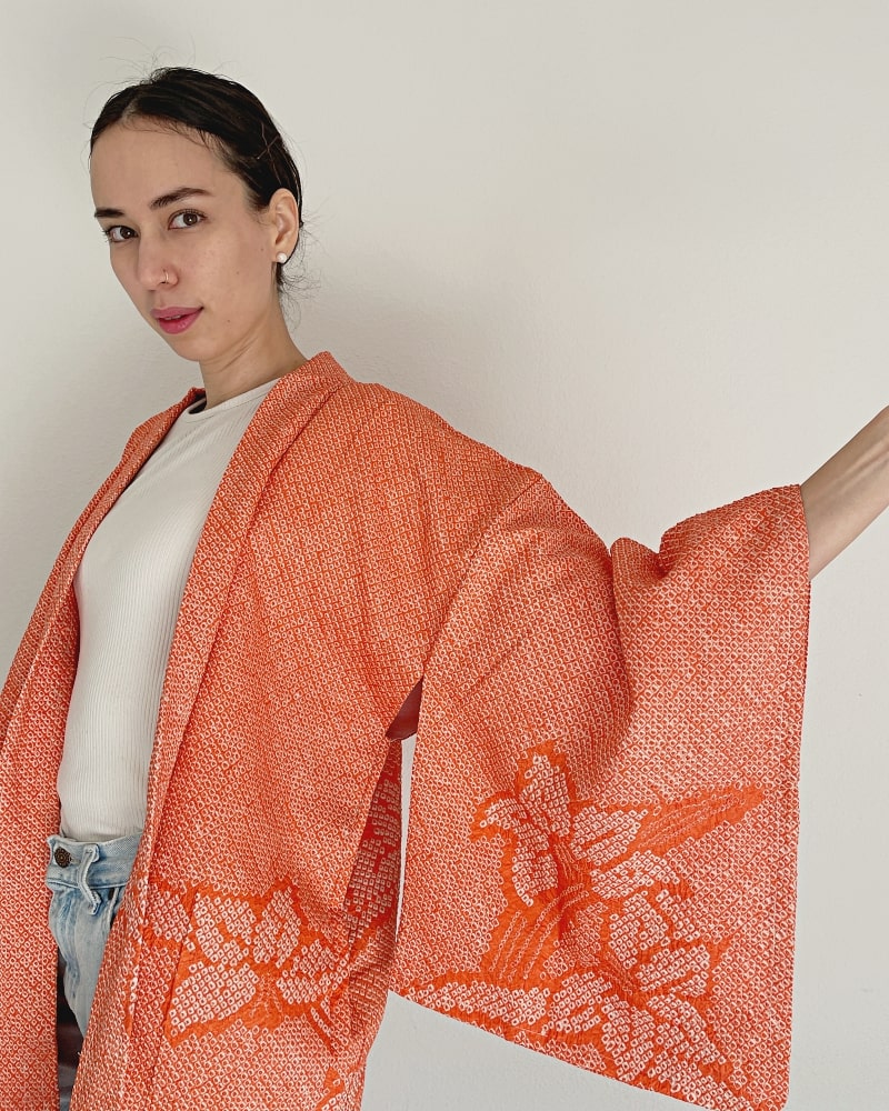 Beautiful Narcissus Haori Kimono Jacket by Kimono zen brand, showing a woman's upper body wearing a beautiful autumn-colored shibori fabric with white cut sleeves and jeans.