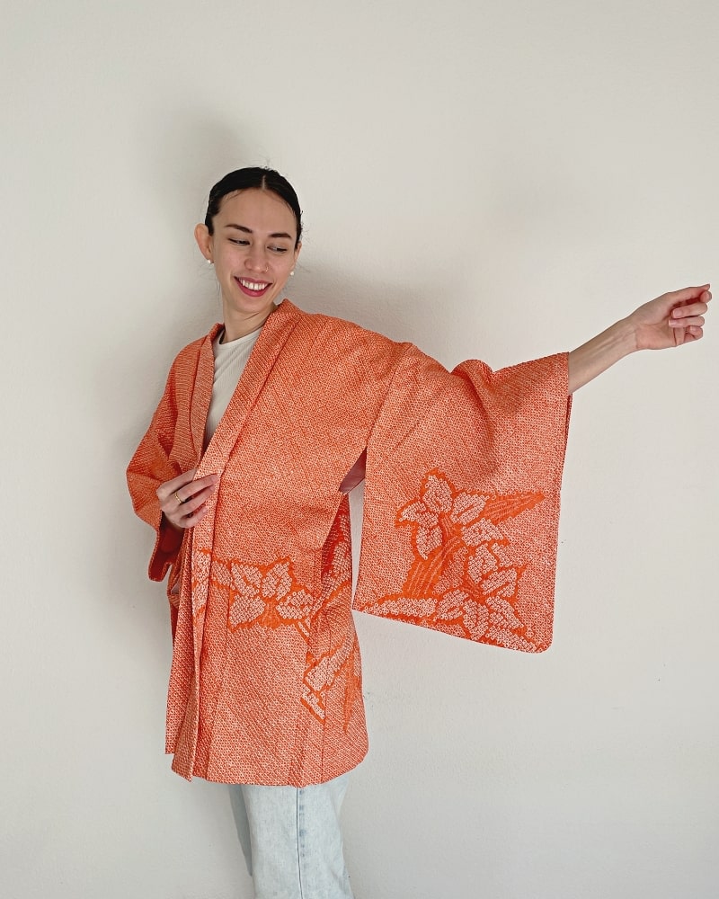 Beautiful Narcissus Haori Kimono Jacket by Kimono zen brand, showing a woman's upper body wearing a beautiful autumn-colored shibori fabric with white cut sleeves and jeans.