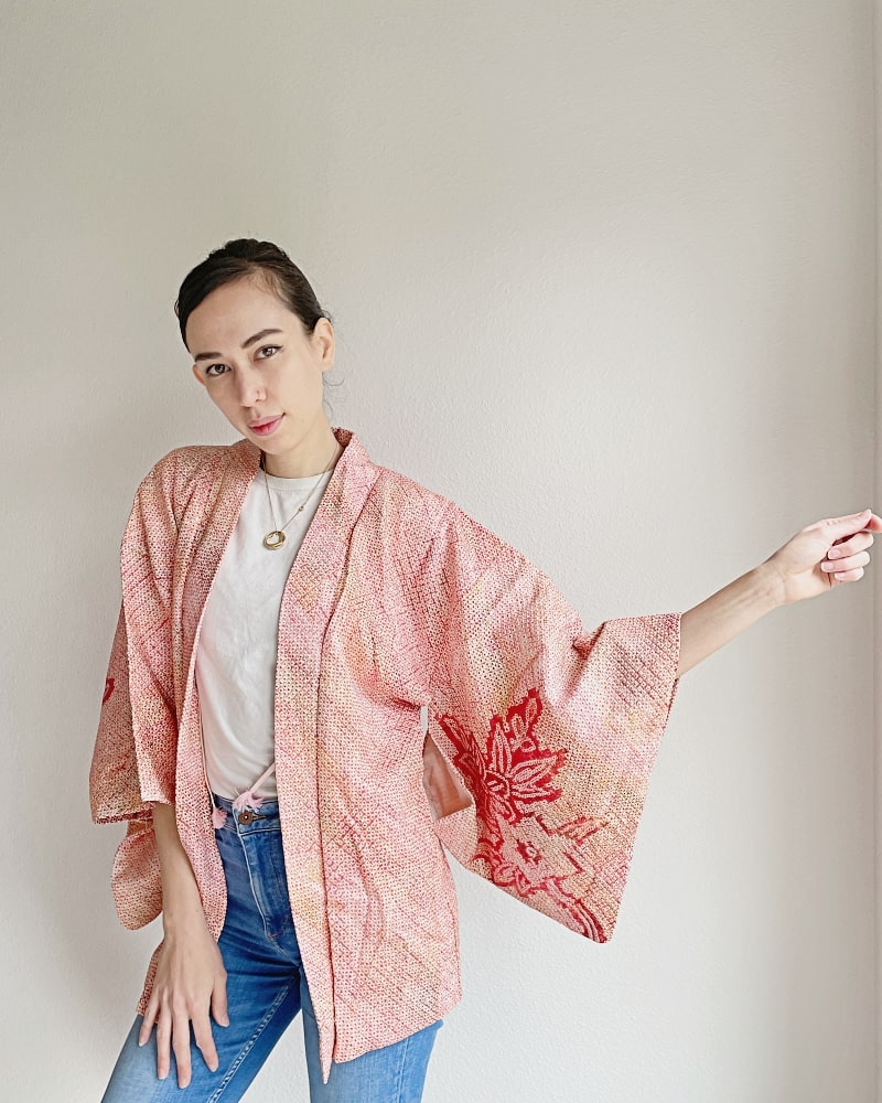 A woman wearing a pinkish shibori fabric with a plum pattern on it with a white T-shirt and jeans.