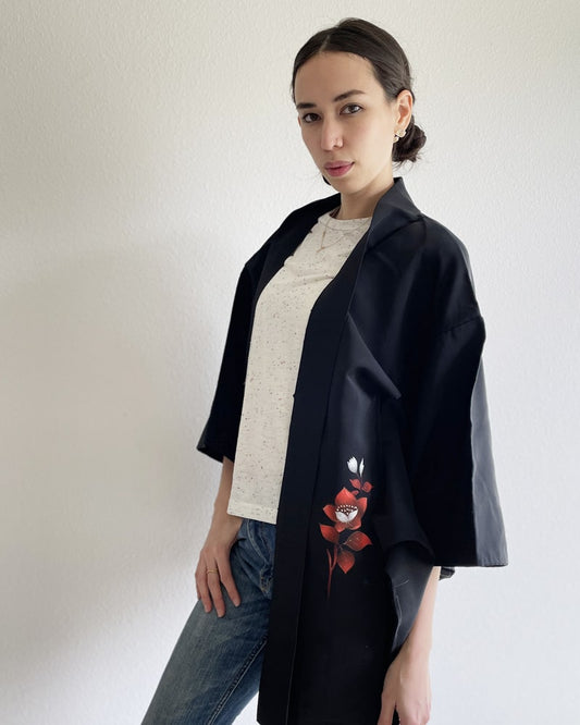 Kimono zen brand Bellflower Black Haori Kimono Jacket, a woman's upper body wearing a kimono jacket with a bright red plum pattern on a black fabric with a white T-shirt and jeans.