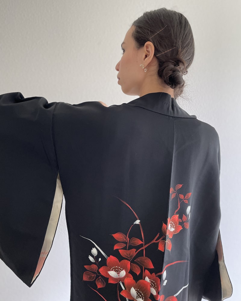Kimono zen brand Bellflower Black Haori Kimono Jacket, a woman wearing a kimono jacket with a bright red plum pattern on black fabric with a white T-shirt and jeans, upper back view