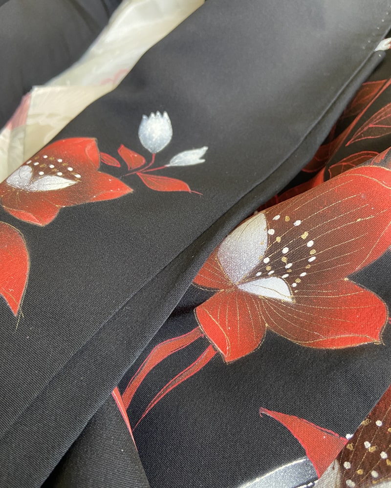 Enlarged image of a kimono patterned with bright red plum blossoms on black fabric.