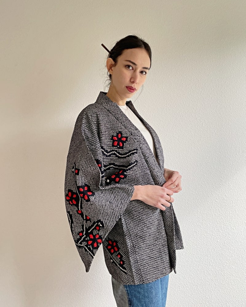 Kimono zen brand Black Cherry Blossom Shibori Haori Kimono Jacket, a woman wearing a black shibori fabric jacket with a bright red plum pattern on the upper body with a white cut and jeans.