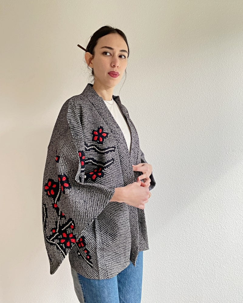 Kimono zen brand Black Cherry Blossom Shibori Haori Kimono Jacket, a woman wearing a black shibori fabric jacket with a bright red plum pattern on the upper body with a white cut and jeans.