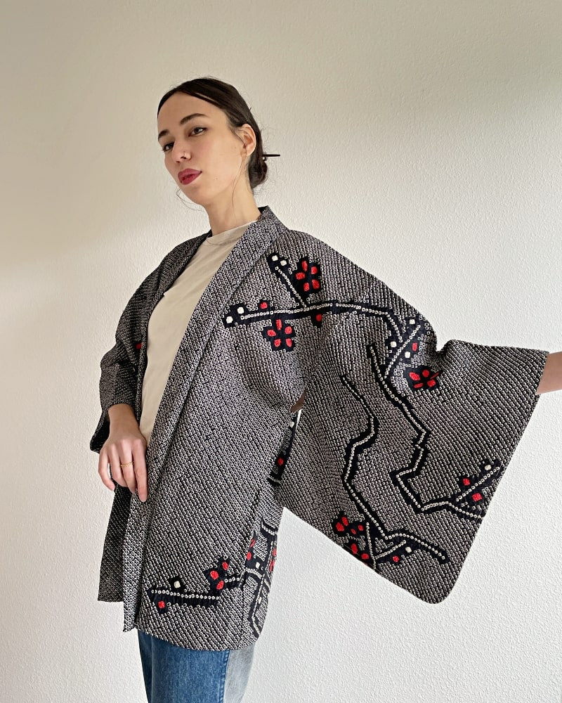 Kimono zen brand Black Cherry Blossom Shibori Haori Kimono Jacket, a woman wearing a black shibori fabric jacket with a bright red plum pattern on the upper body with a white cut and jeans.