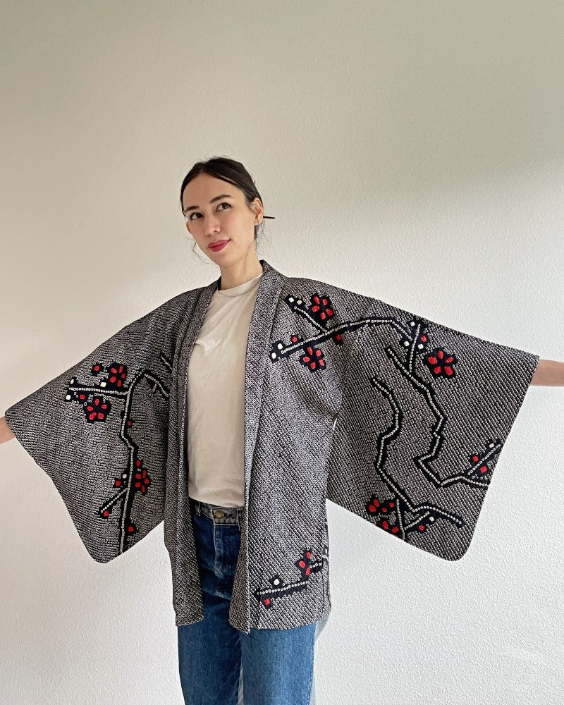 Kimono zen brand Black Cherry Blossom Shibori Haori Kimono Jacket, a woman wearing a black shibori fabric jacket with a bright red plum pattern on the upper body with a white cut and jeans.