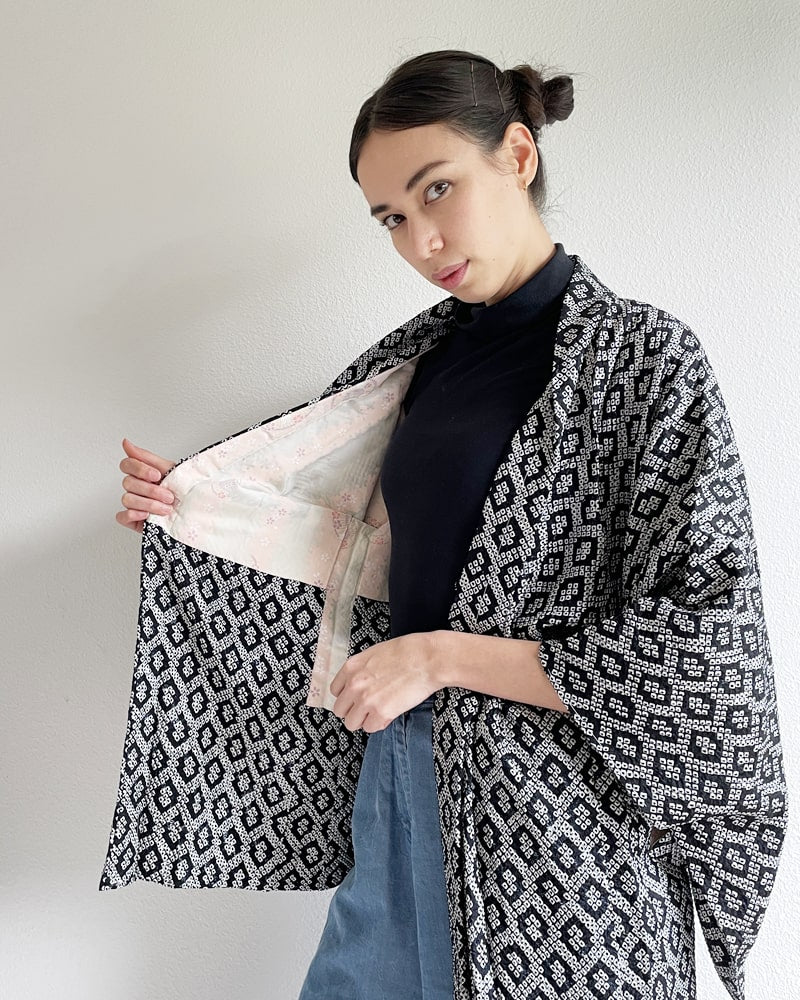 Black Shibori Haori Kimono Jacket of the Kimono zen brand, black in color with diamond-shaped pattern all over, worn by a woman with a black turtleneck and jeans on her upper body