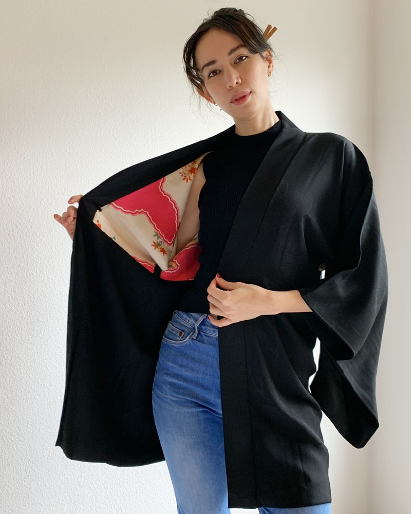 Kimono zen brand Black with Aurora Glitter Thread Haori Kimono Jacket, black with red patterned lining, worn with a black cut and jeans.