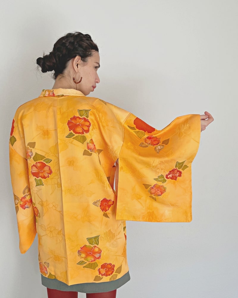 Back view of a woman wearing a Kimono zen brand Bright Orange Floral Haori Kimono Jacket with a white T-shirt, gray skirt, and red/purple tights