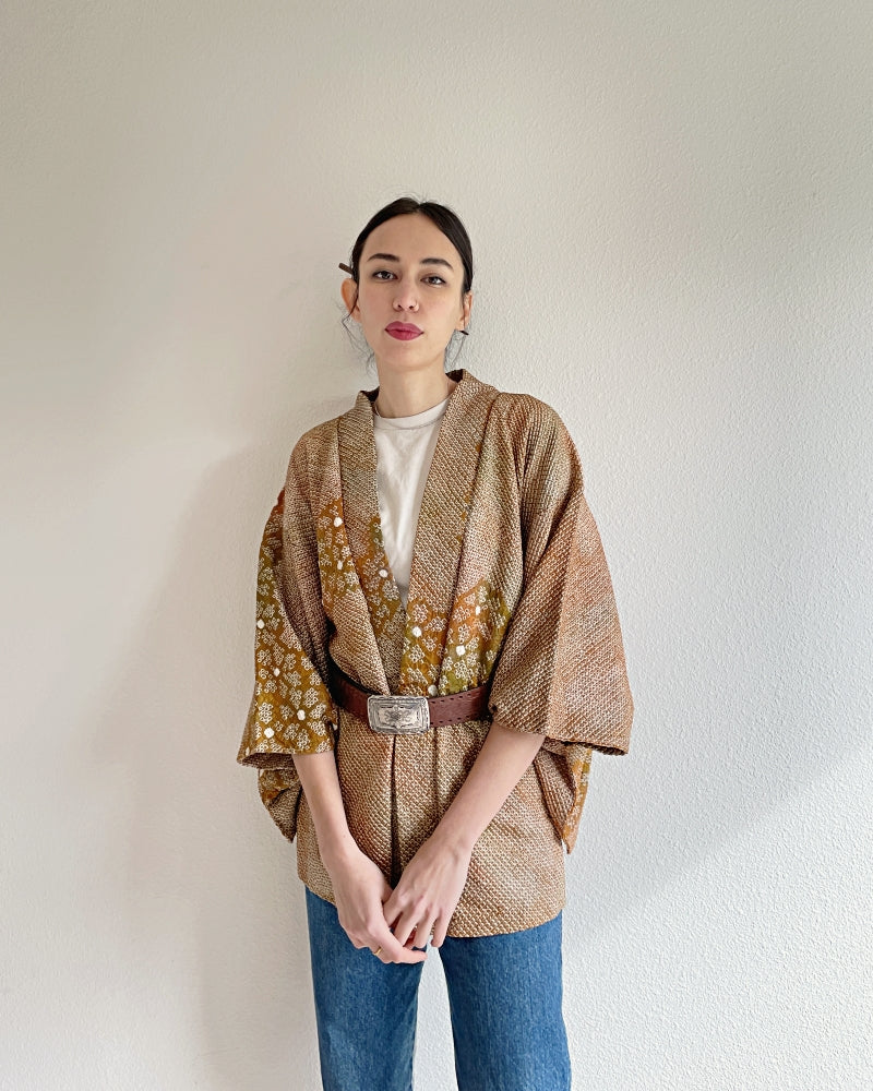 A woman wearing a shibori kimono haori, brown in color, with a plum flower design and a leather belt
