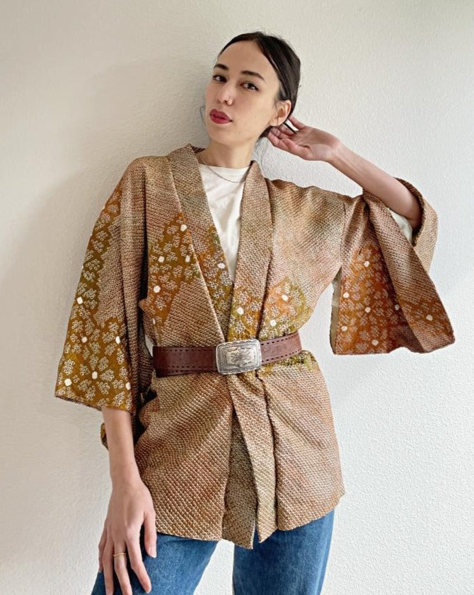 A woman wearing a shibori kimono haori, brown in color, with a plum flower design and a leather belt