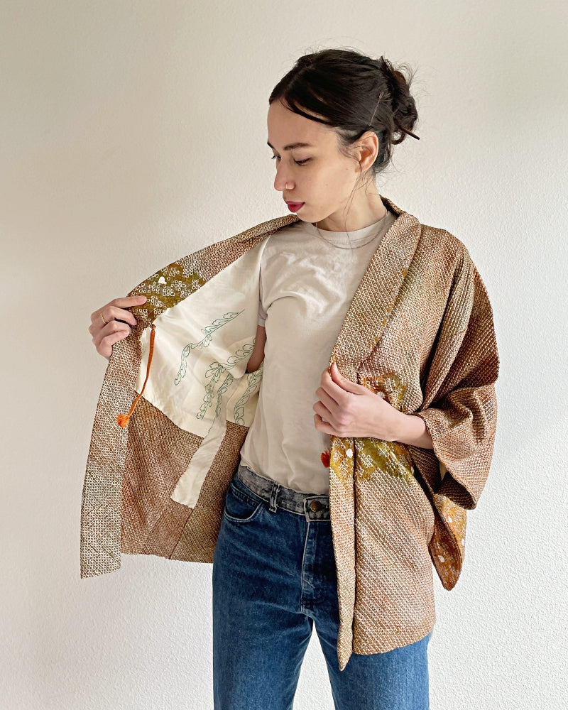 A woman wearing a shibori kimono haori, brown in color, with a plum flower design and a leather belt